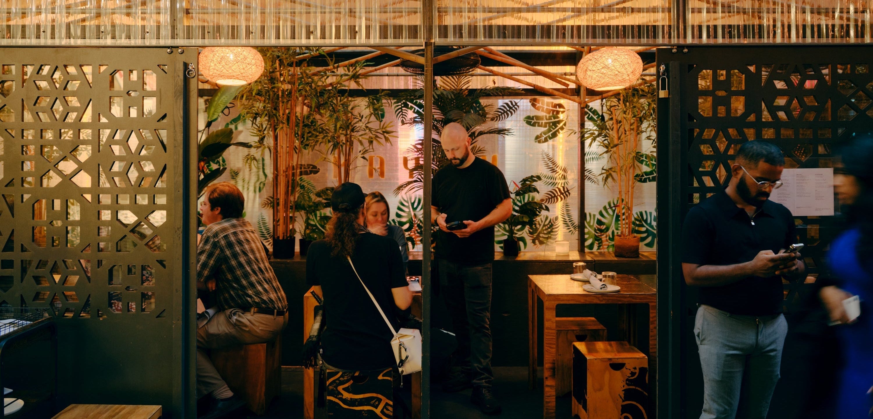 An outdoor dining pavilion by re-ply, at Wayan restaurant in Spring Street, NYC, with decorative laser-cut winter enclosure, warm hanging pendant lights, heaters and indoor plants, with several people seated and standing in a real urban setting. Image credit: Tom Ross Photography